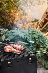 raw meat grilling on barbecue grid and coal pieces outside