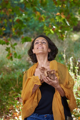  Latin brunette woman with a black t-shirt in a forest with dry leaves and autumnal colors, the sun enters between the branches of the trees.