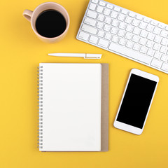 Fototapeta na wymiar Flat lay design of modern office desk mock up with notebook, laptop, smartphone, pen and cup of coffee on yellow background with copy space. Top view. Workspace and business concept.