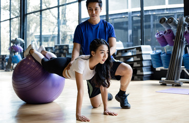 Fototapeta na wymiar Asian woman playing yoga by yoga ball with trainer man.