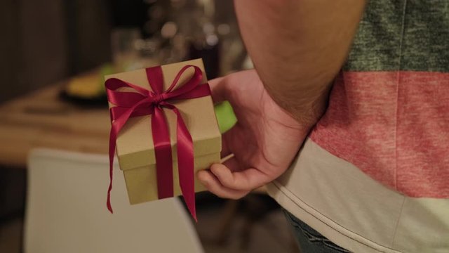 A man holds a gift box with a red ribbon behind his back. Getting ready to make a surprise.