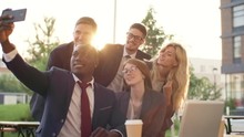 Medium shot of cheerful young business people of different ethnicities smiling and posing for camera when taking group selfie on smartphone