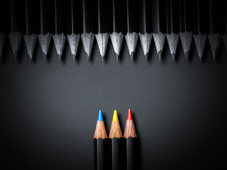 Red, yellow and blue pencil laying against the row of the black pencils on a black beckgtound. Not...