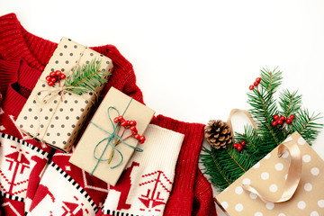 Christmas flat lay with a warm knitted patterned sweater, gift boxes and fir branches on a white background with copy space for text.