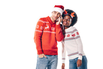 Fototapeta premium happy interracial couple in santa hat and deer horns talking on smartphone, isolated on white