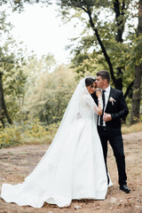 Naklejka premium Happy newlywed couple walking in the park. Beautiful bride with her husband in the park. They are walking. Close up of a newlywed couple, a bride with a beautiful hair style and make up. 