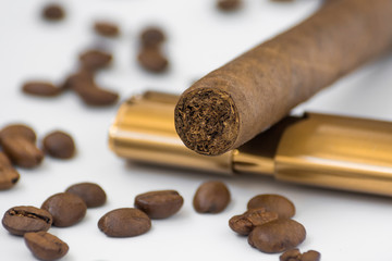 Closeup photo of a cigar and a lighter lying on a white table among coffee beans
