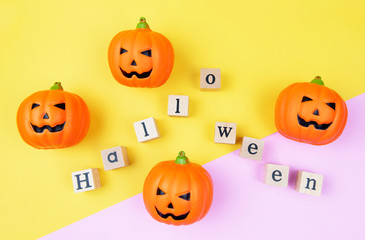 Above of four orange pumpkin items with Halloween wooden block word on pink and yellow background. minimal style. flat lay. Top view photo.