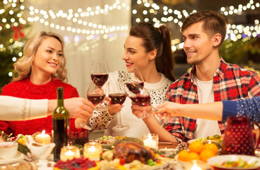 holidays and celebration concept - happy friends having christmas dinner at home, drinking red wine and clinking glasses