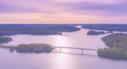 Aerial view of modern bridge with cars across blue lake Saimaa at summer sunset time. Beautiful sky with clouds. Finland