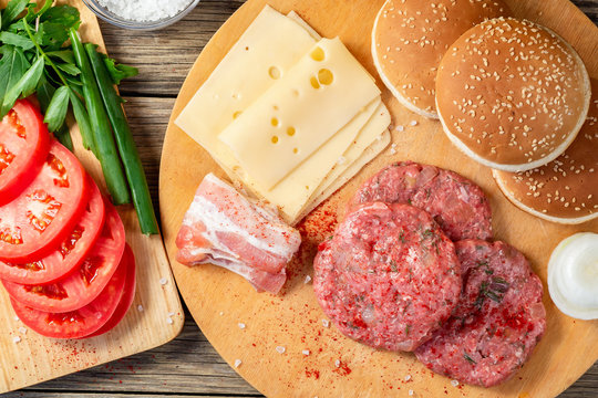 Process of cooking homemade burgers, meatballs, tomatoes, cheese and other ingredients on a wooden table, flat lay, top view