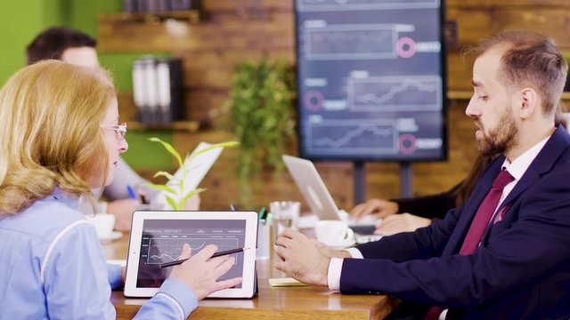 Middle age female team lider standing near the table giving direction to her young coworker