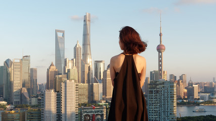 Rear view of beautiful young brunette woman in sexy black dress posing on top of mansion roof with...