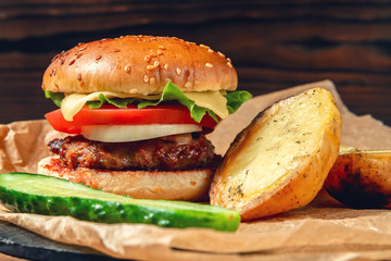 Fresh homemade burger and baked potatoes with cucumber on the table