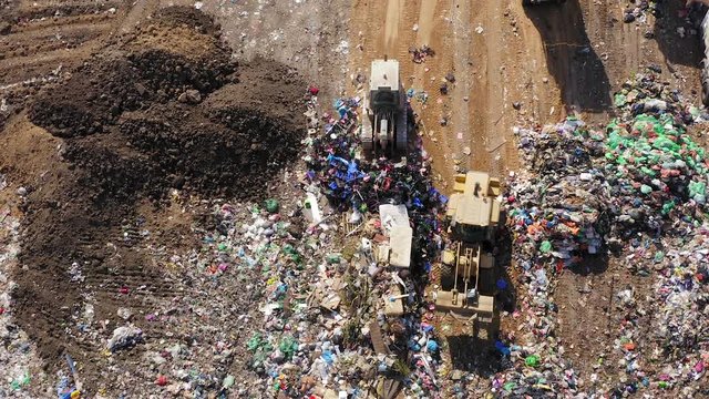 Top down aerial footage of a Municipal Solid waste Landfill during collecting, sorting and pressing work, with a massive flock of birds.