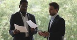 Focused african and caucasian partners discussing project holding papers tablet
