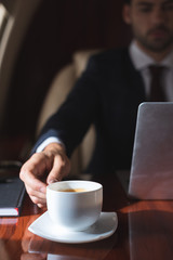 selective focus of businessman holding cup of coffee in plane with laptop