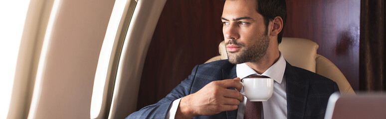 confident businessman in suit drinking coffee in airplane during business trip