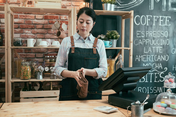 asian chinese woman barista in coffee shop clean wooden table in bar. Pretty female waitress stand...