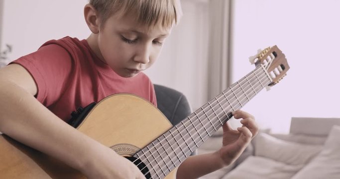Young boy with a guitar. Boy of 8 years plays the classical guitar. The caucasian child learns to play the guitar. .Real time. Zoom in. Natural lighting. Low angle view.