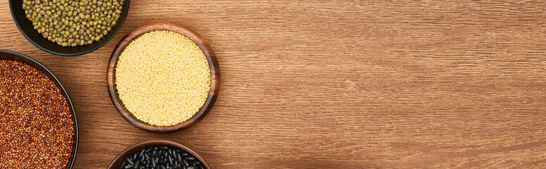 panoramic shot of bowls with couscous, green and black beans and buckwheat on wooden surface