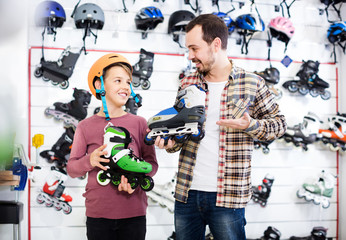 Male shop assistant helping boy to choose roller-skates in sports store