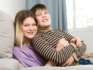 Portrait of young woman and smiling son hugging at sofa