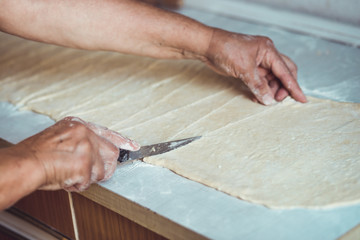 Female hands cutting dough with knife. Process of making croissant rolls