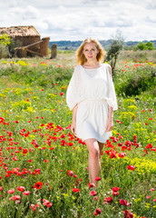 Naklejka na ściany i meble Young woman in white dress walking through a poppies plant