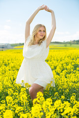 Naklejka na ściany i meble Happy girl stretch oneself in rape seed flowers field posing in white dress