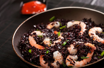 Cooked black rice with shrimps and green onion in a pan on the black background.