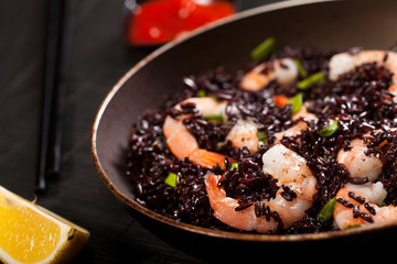 Cooked black rice with shrimps and green onion in a pan on the black background.