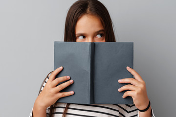 Student girl teenager holding a book in her hands over a grey background.