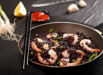 Cooked black rice with shrimps and green onion in a pan on the black background.