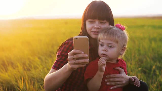 happy family funny a mom holds daughter take selfie on smartphone playing silhouette at sunset slow motion. little girl and woman mom play are photographed outdoors sunlight selfie on lifestyle the