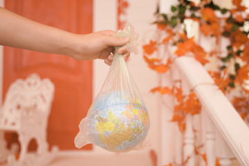 horizontal photo of a teenager's hand holding a planet in a bag. concept of planet earth suffering and suffocating from plastic and overheating.