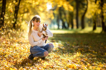 Fototapeta premium girl sits and relax on the ground in the autumn forest and plays with Yorkshire Terrier small dog