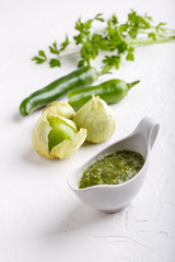 Tomatillo salsa verde. Bowl of spicy green sauce on white table, mexican cuisine.