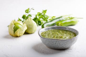 Tomatillo salsa verde. Bowl of spicy green sauce on white table, mexican cuisine. - obrazy, fototapety, plakaty