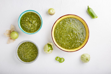 Tomatillo salsa verde. Bowl of spicy green sauce on white table, mexican cuisine. Top view. Copy space.