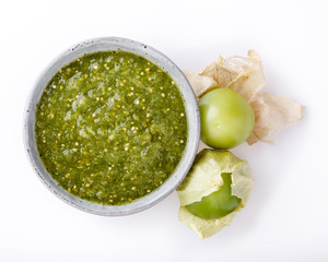 Tomatillo salsa verde. Bowl of spicy green sauce on white table, mexican cuisine. Top view.