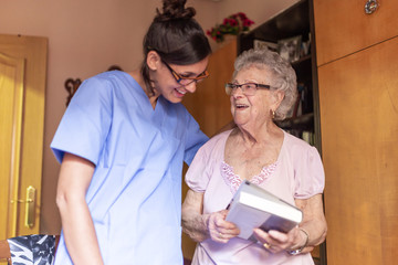 Happy Senior woman with her caregiver at home holding a book and smiling. Senior home care concept.