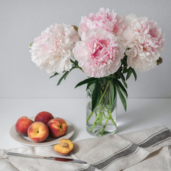 Ripe peaches on a plate and a bouquet of peonies