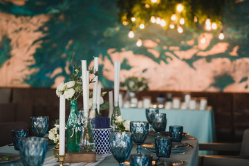 Coziness and style. Modern event design. Table setting at wedding reception. Floral compositions with beautiful flowers and greenery, candles, laying and plates on decorated table.