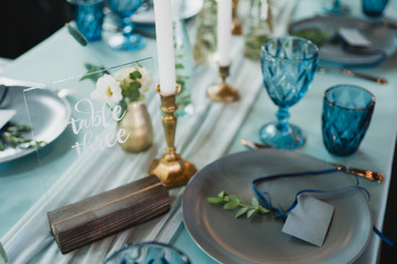 Coziness and style. Modern event design. Table setting at wedding reception. Floral compositions with beautiful flowers and greenery, candles, laying and plates on decorated table.