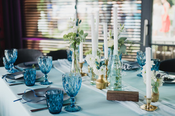 Coziness and style. Modern event design. Table setting at wedding reception. Floral compositions with beautiful flowers and greenery, candles, laying and plates on decorated table.