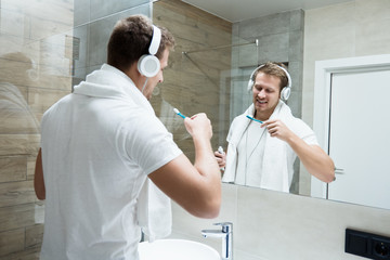 young handsome man in headphones brushing teeth in bathroom