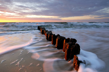 Zachód słońca na wybrzeżu Morza Bałtyckiego,fale oblewają falochron na piaszczystej plaży,Kołobrzeg,Polska.