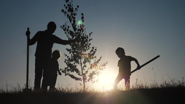 happy family of farmers a silhouette concept slow motion video. dad son and daughter children plant and water the tree outdoors in the park lifestyle . happy family little girl and boy works in garden