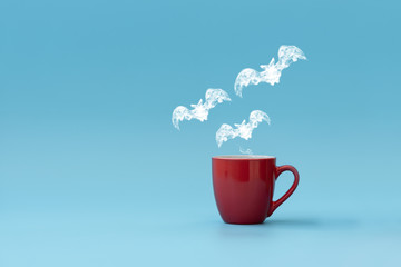 Steam in three bats shape flying from coffee cup against blue background. Morning drink. Halloween celebration concept. Copy space
